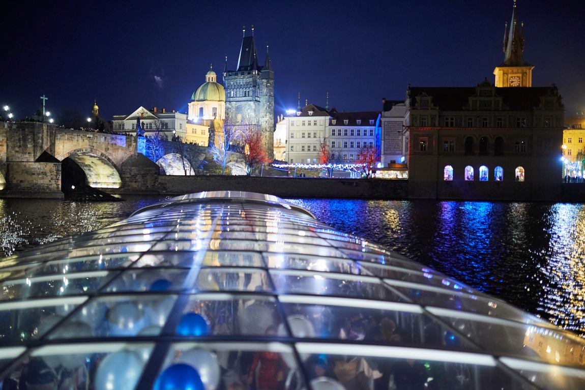 The glass roof of Bohemia Rhapsody at night facing illuminated Charles Bridge