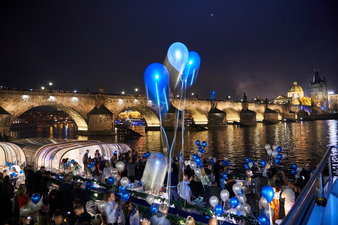 Guests with balloons on deck at night in front of illuminated Charles Bridge