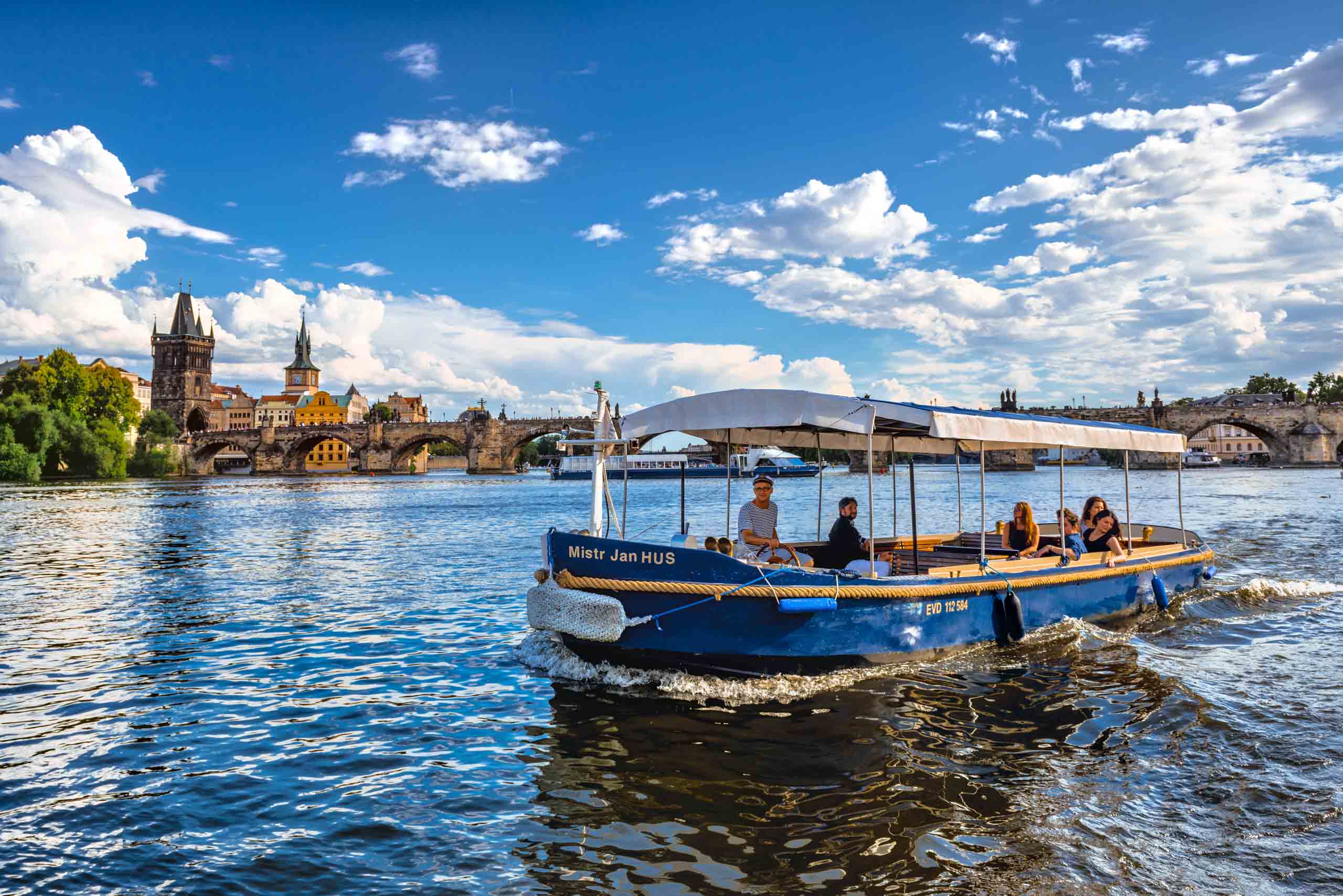 Mistr Jan Hus s cestujícími zblízka, v pozadí Karlův most